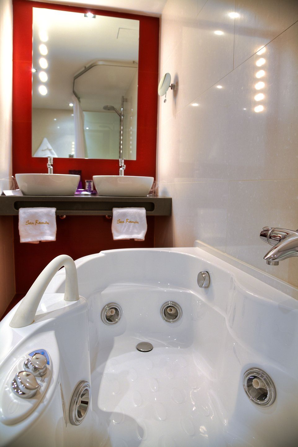 A bathroom with a large white bathtub, two sinks, a mirror, and a red accent wall.