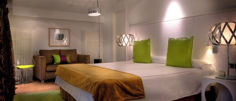 A modern hotel room with a large bed, a sofa, a chair, and a unique circular side table.