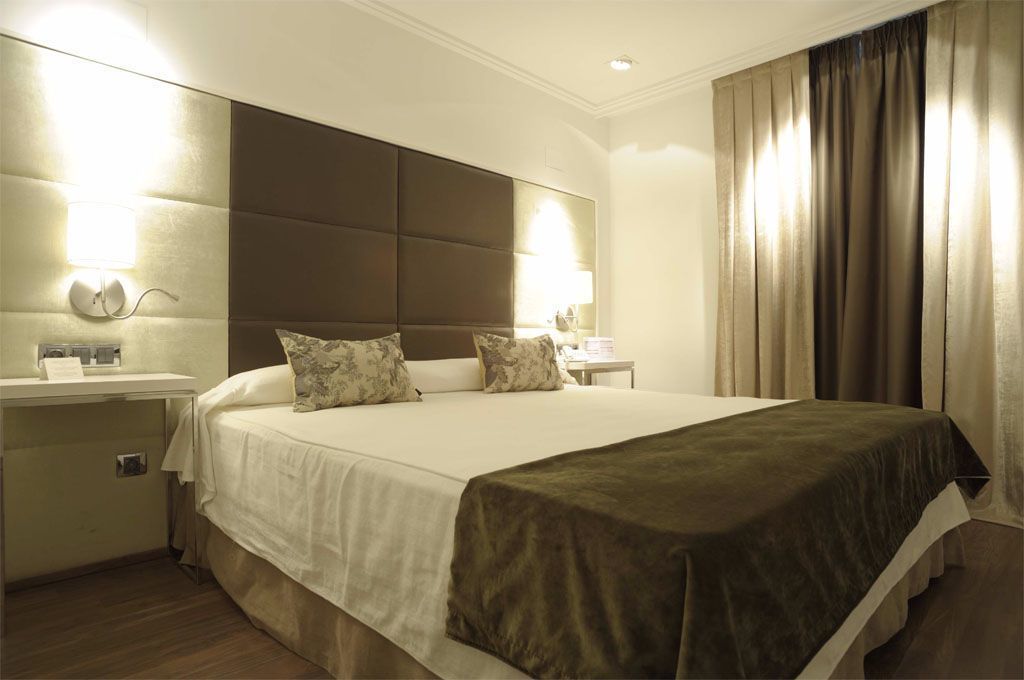 Ein Hotelzimmer mit einem großen Bett, einem Nachttisch, einer Wandlampe und einem Beistelltisch.