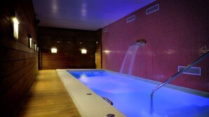 Un área de spa con hidromasaje, suelo de madera y pared revestida de azulejos con fuente de agua.