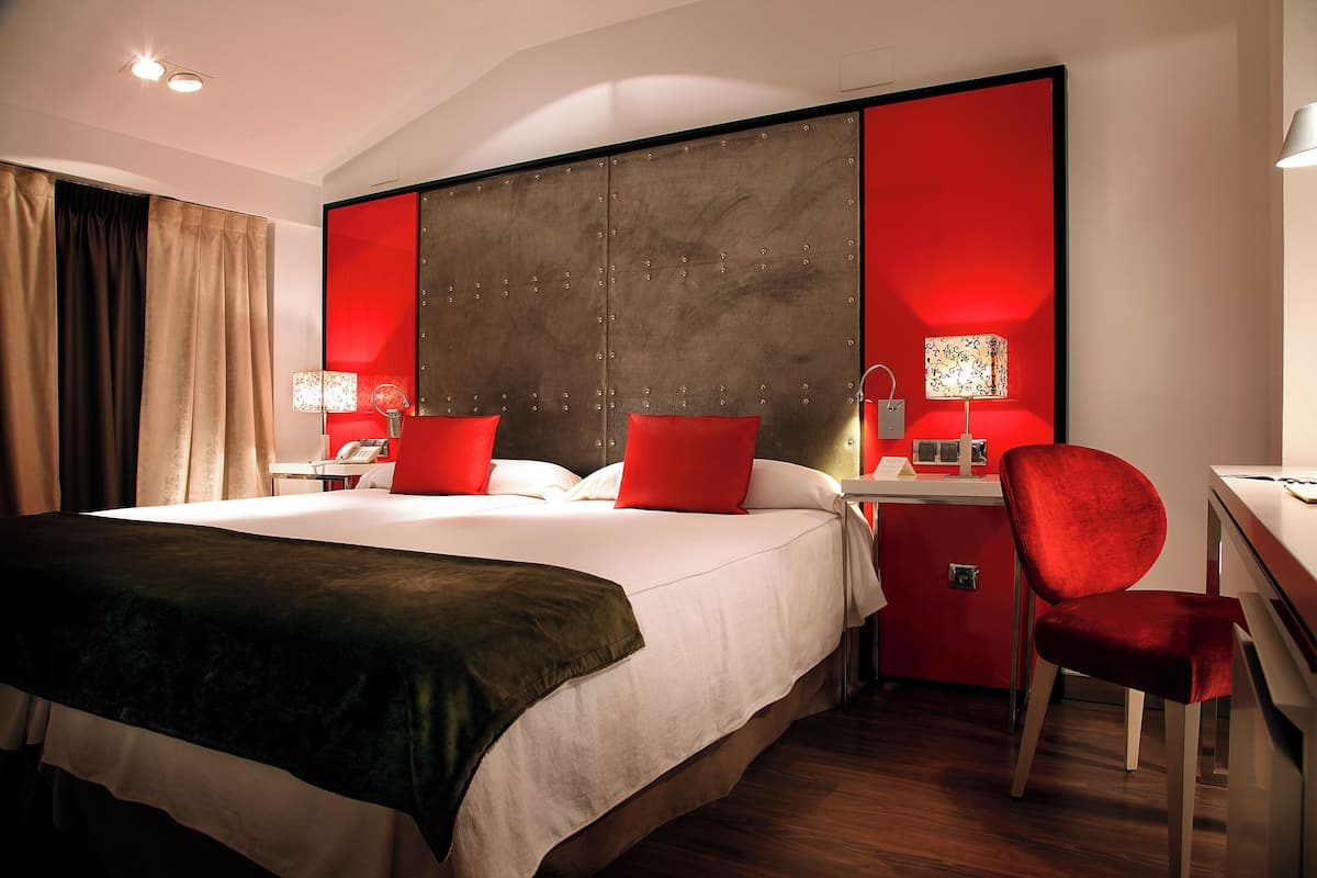 A hotel room with a large bed, a desk with a chair, and two bedside lamps.