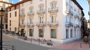 Un edificio de varios pisos con balcones, una calle en su parte frontal y una zona adoquinada.