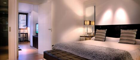 A modern bedroom with a large bed, a bench, a desk, and a TV.