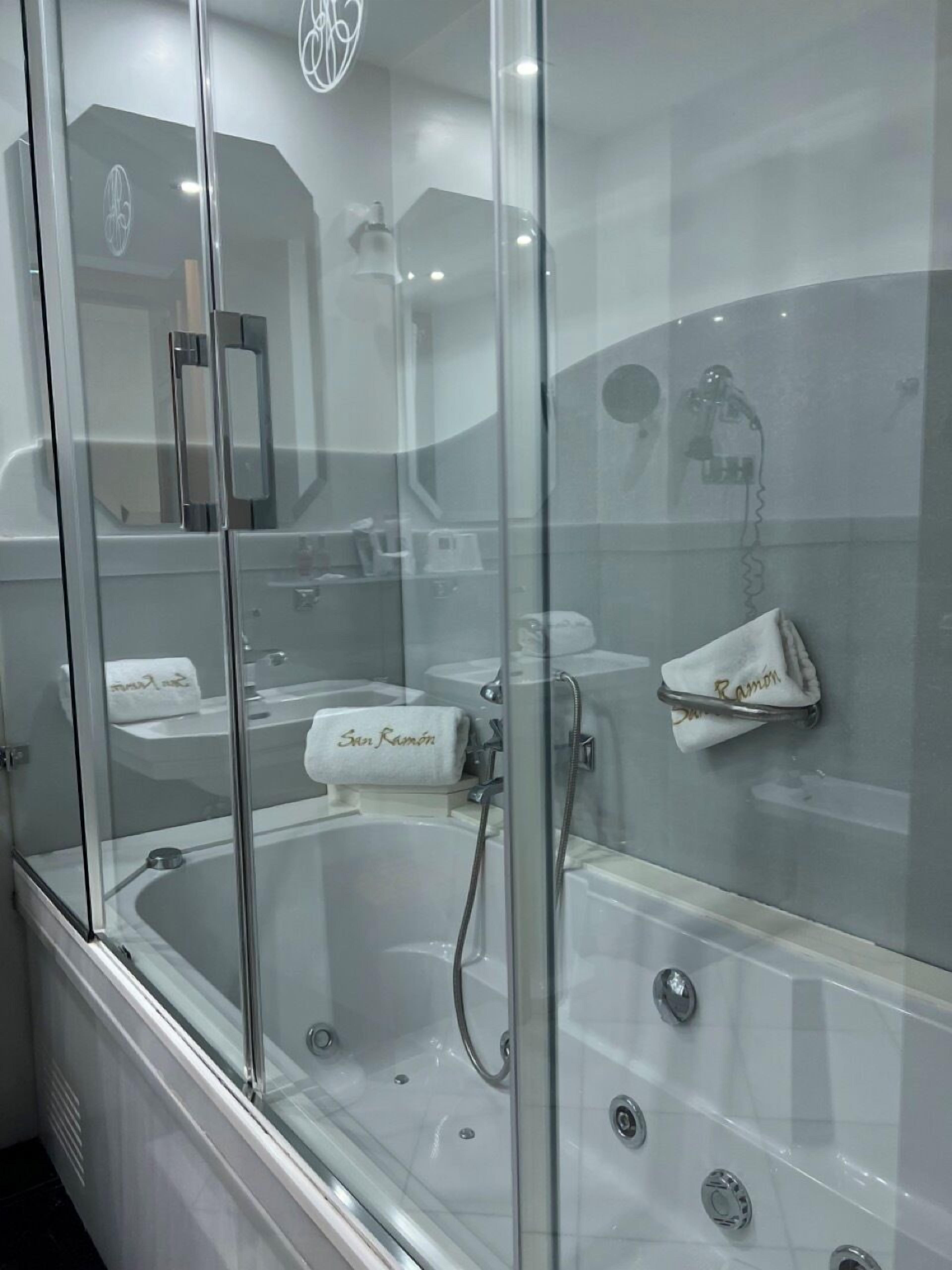 Un bagno moderno con doccia a parete in vetro, una vasca da bagno ampia e un WC chiuso da vetro.