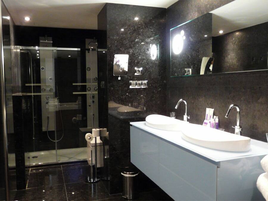 Un baño moderno con ducha de vidrio, lavamanos doble y un espejo grande.