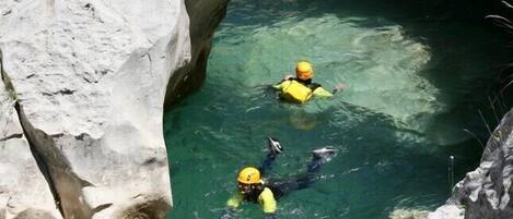A group of people in yellow helmets and life vests swimming in a narrow, rocky waterway.