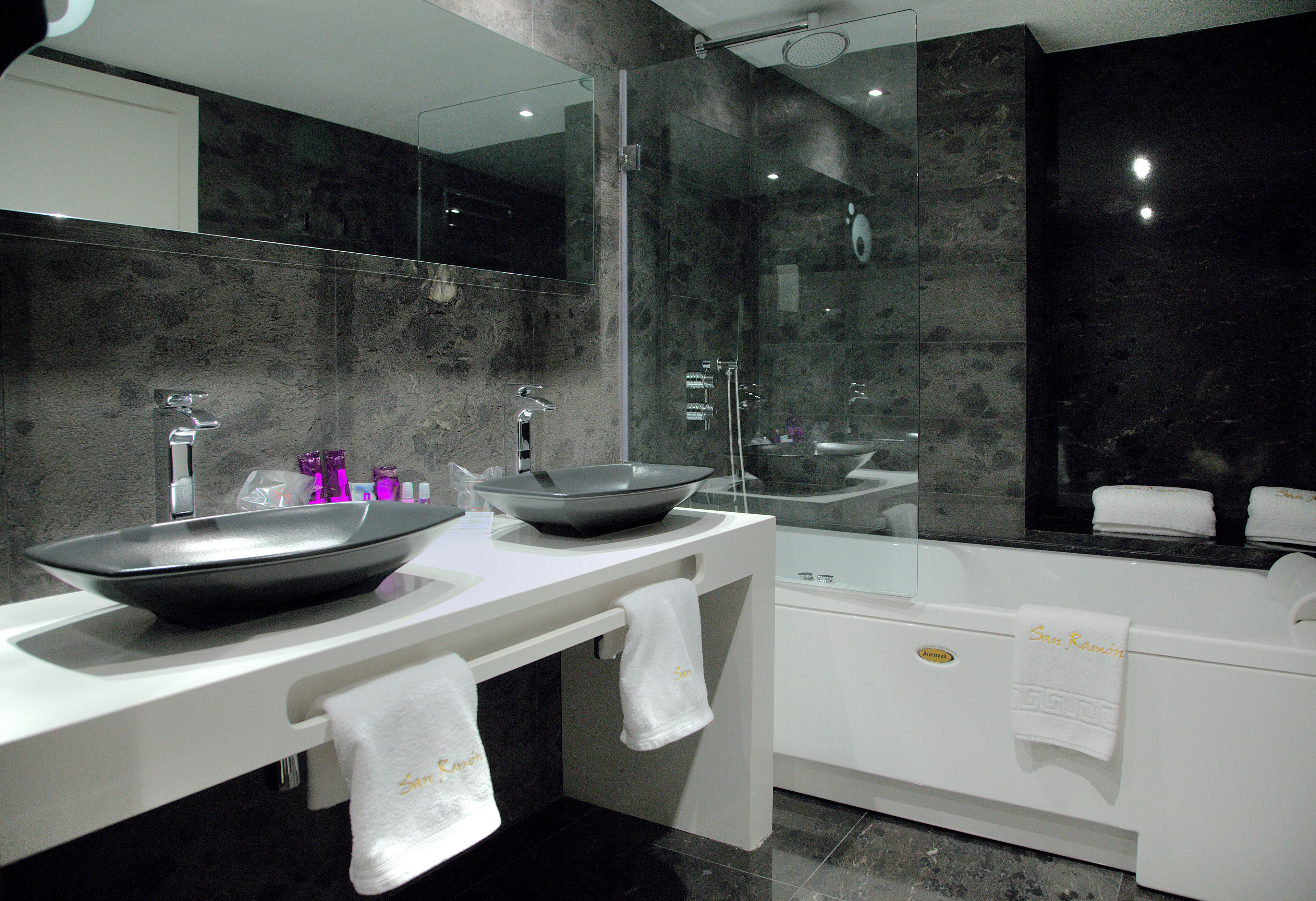 Une salle de bain moderne avec un grand miroir, deux vasques de grande taille, une baignoire et des serviettes accrochées au mur.