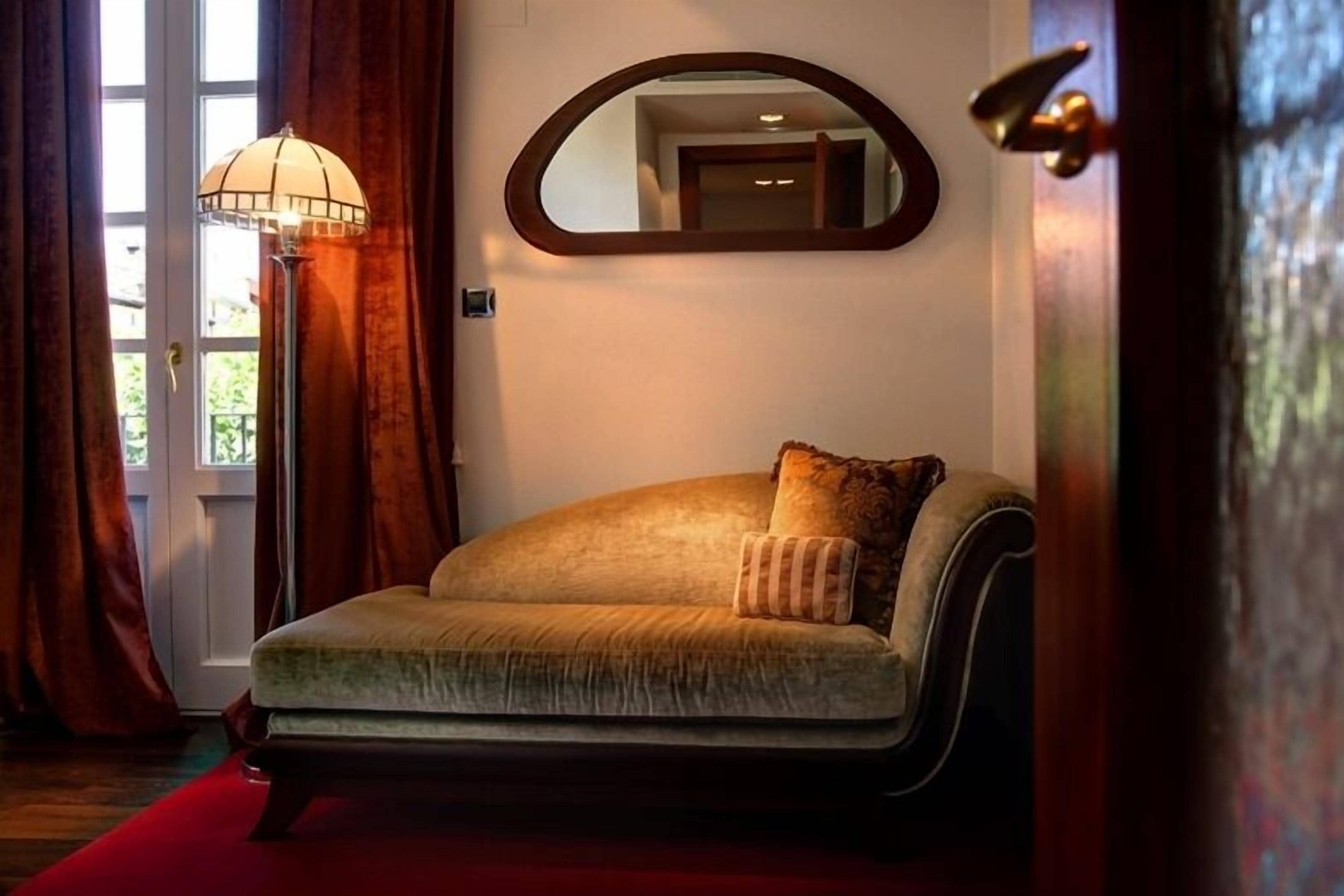 A room with a sofa, a mirror, and a lamp.