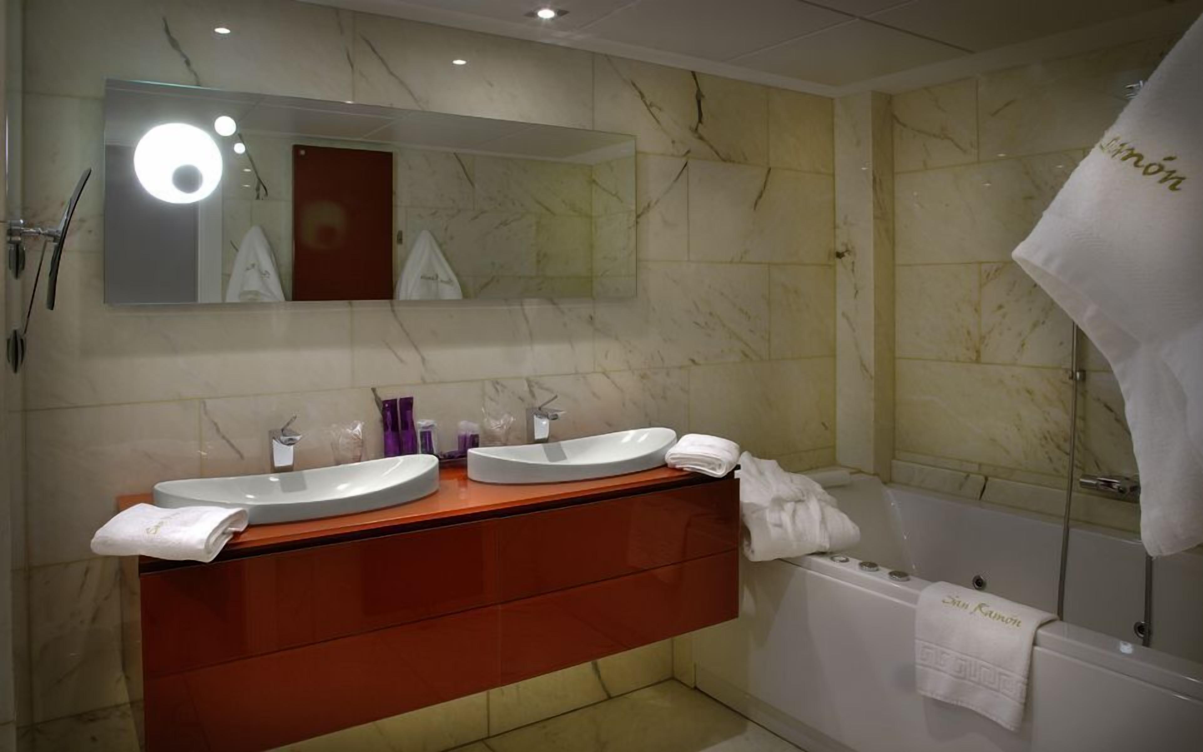 A bathroom with two sinks, a mirror, and a bathtub.