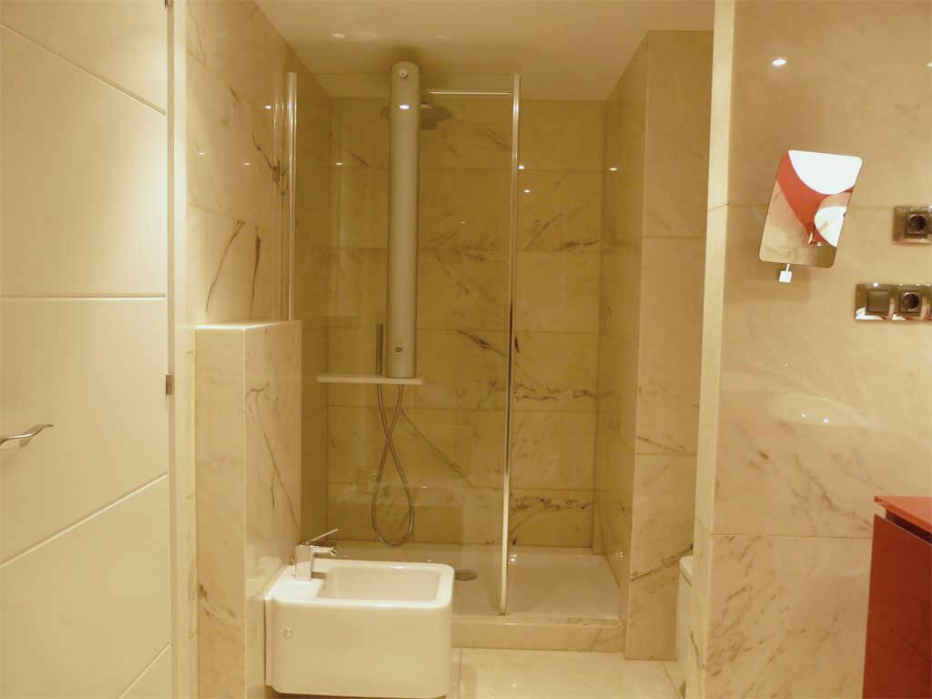 Une salle de bain moderne avec une douche à parois de verre, un lavabo blanc et des murs en marbre.