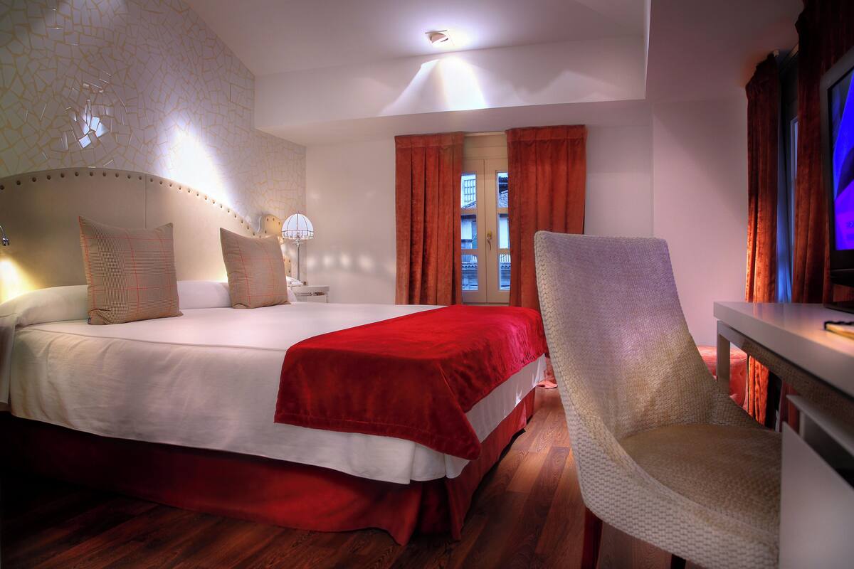 A hotel room with a large bed, a chair, a desk, and a window with curtains.