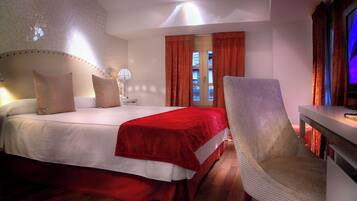 Ein Hotelzimmer mit einem großen Bett, einem Sessel, einem Schreibtisch und einem Fenster mit Vorhängen.