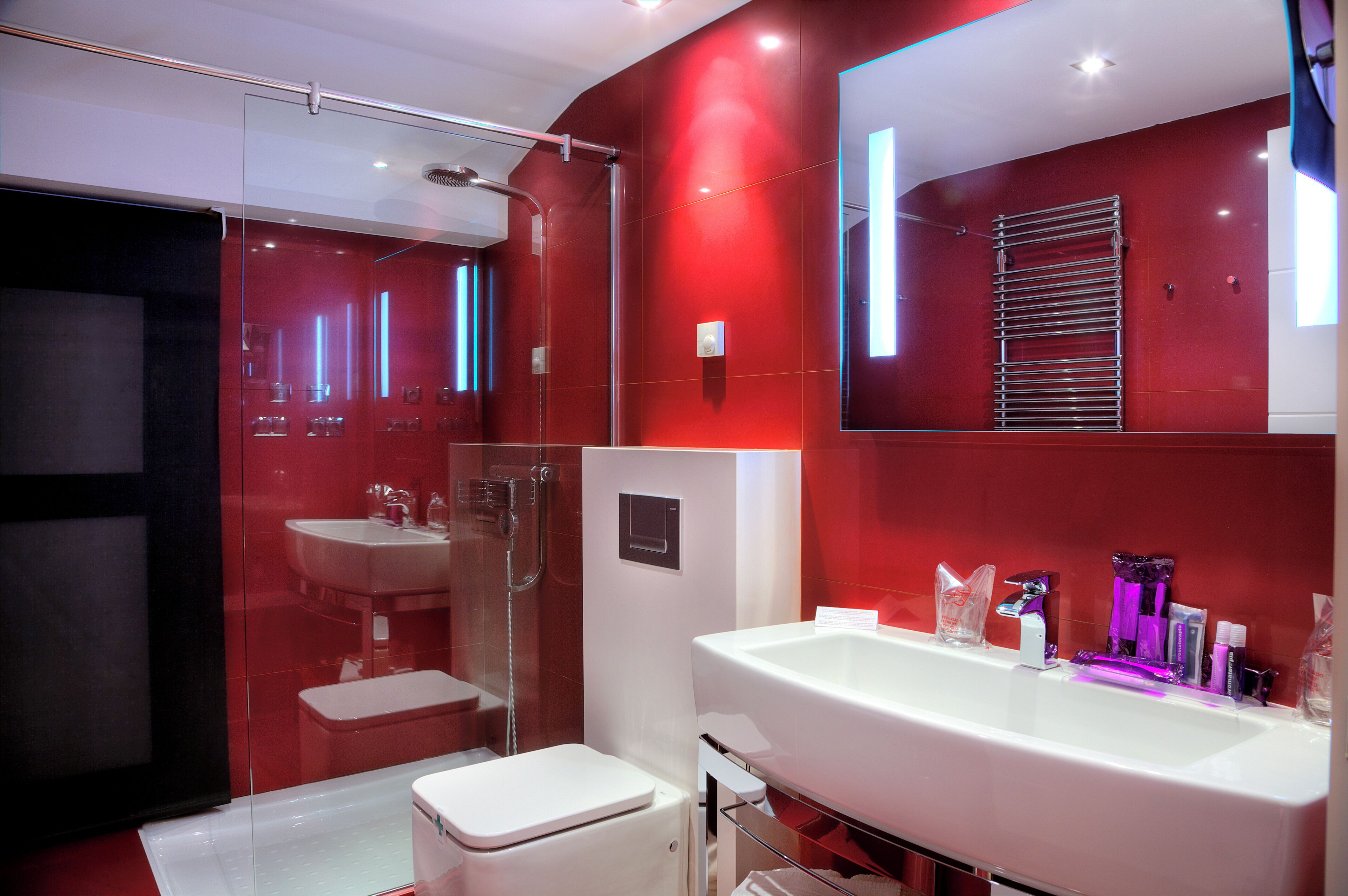 A modern bathroom with a large white sink, a glass shower enclosure, and a red-tiled wall.