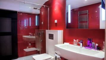 A modern bathroom with a large white sink, a glass shower enclosure, and a red-tiled wall.