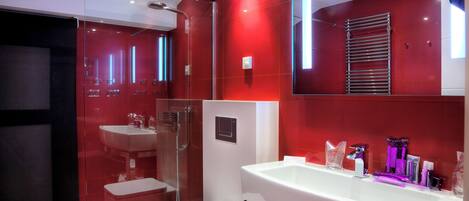 A modern bathroom with a large white sink, a glass shower enclosure, and a red-tiled wall.