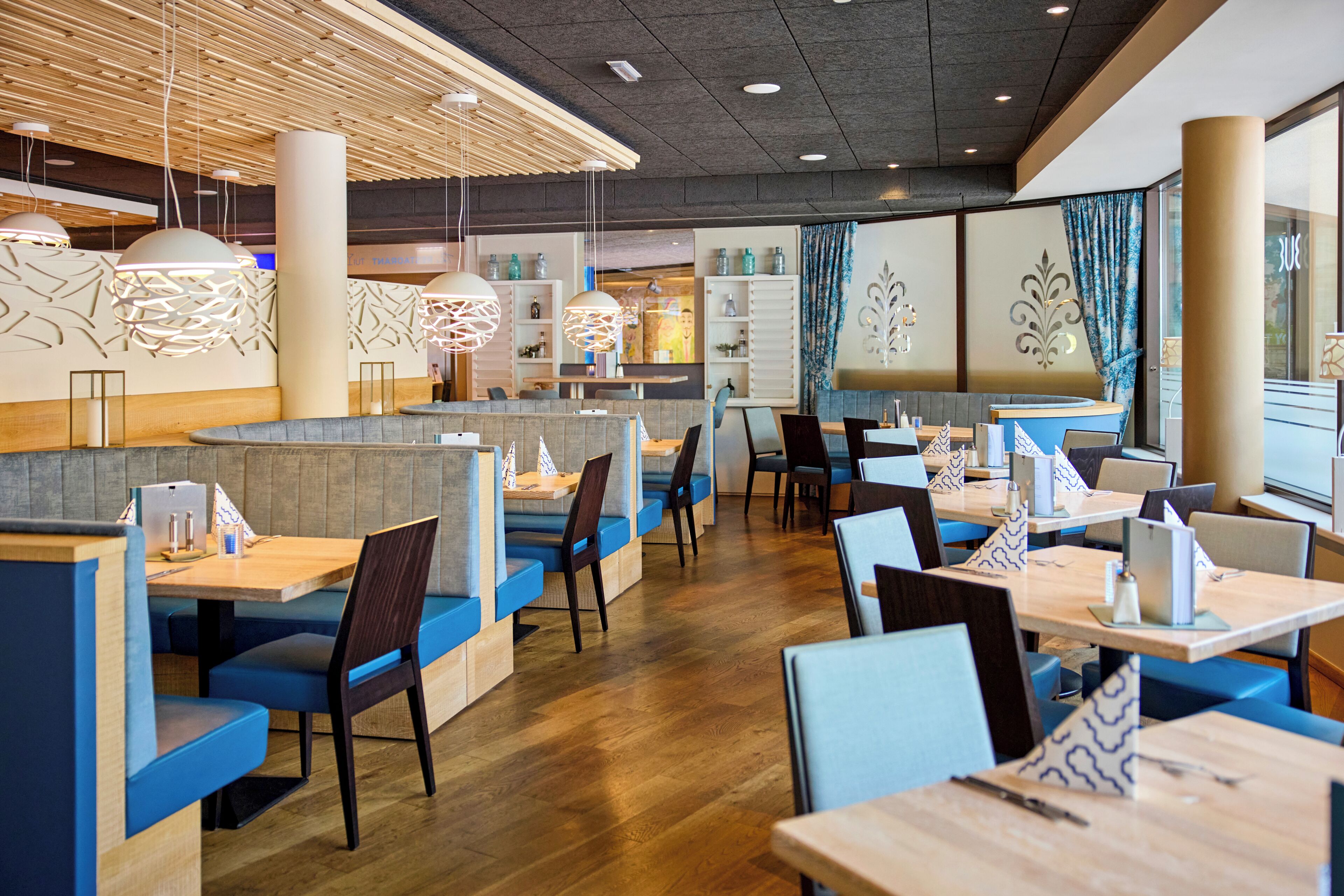 A modern restaurant interior with booths and tables, wooden flooring, and pendant lighting.