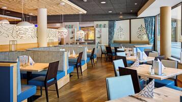 A modern restaurant interior with booths and tables, wooden flooring, and pendant lighting.
