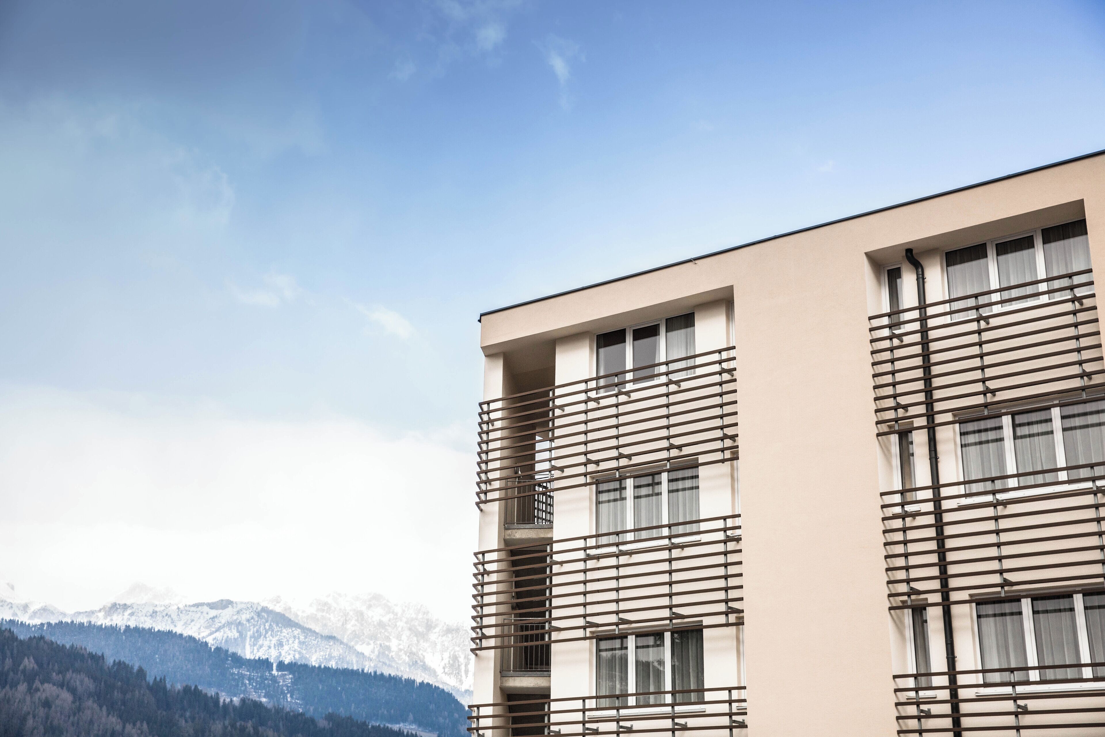 Ein modernes Gebäude mit flachem Dach, großen Fenstern und einem Balkon mit Metallgeländern.