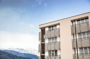 Un edificio moderno con techo plano, ventanas grandes y un balcón con barandillas de metal.