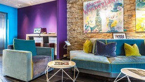 Eine Lobby mit einer Steinwand, einem blauen Sofa, Türkis-Armstühlen und einer violetten Säule.