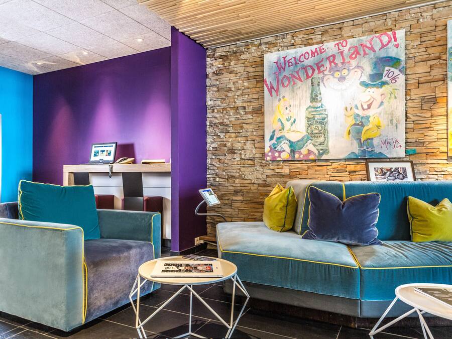 A lobby with a stone wall, a blue sofa, teal armchairs, and a purple pillar.