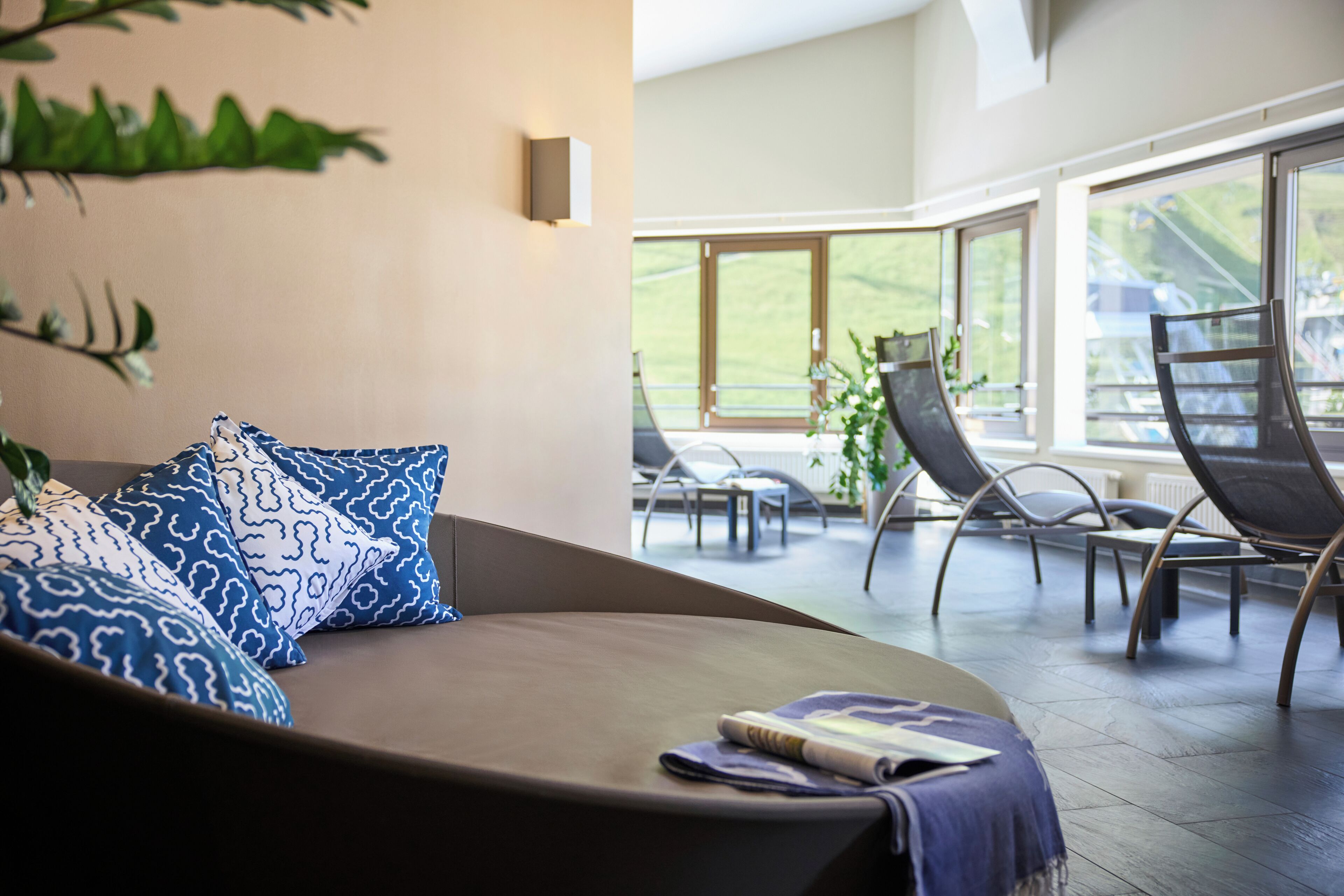 Ein stilvoller Lounge-Bereich mit einer gebogenen Couch, gemusterten Kissen und Blick ins Freie durch große Fenster.