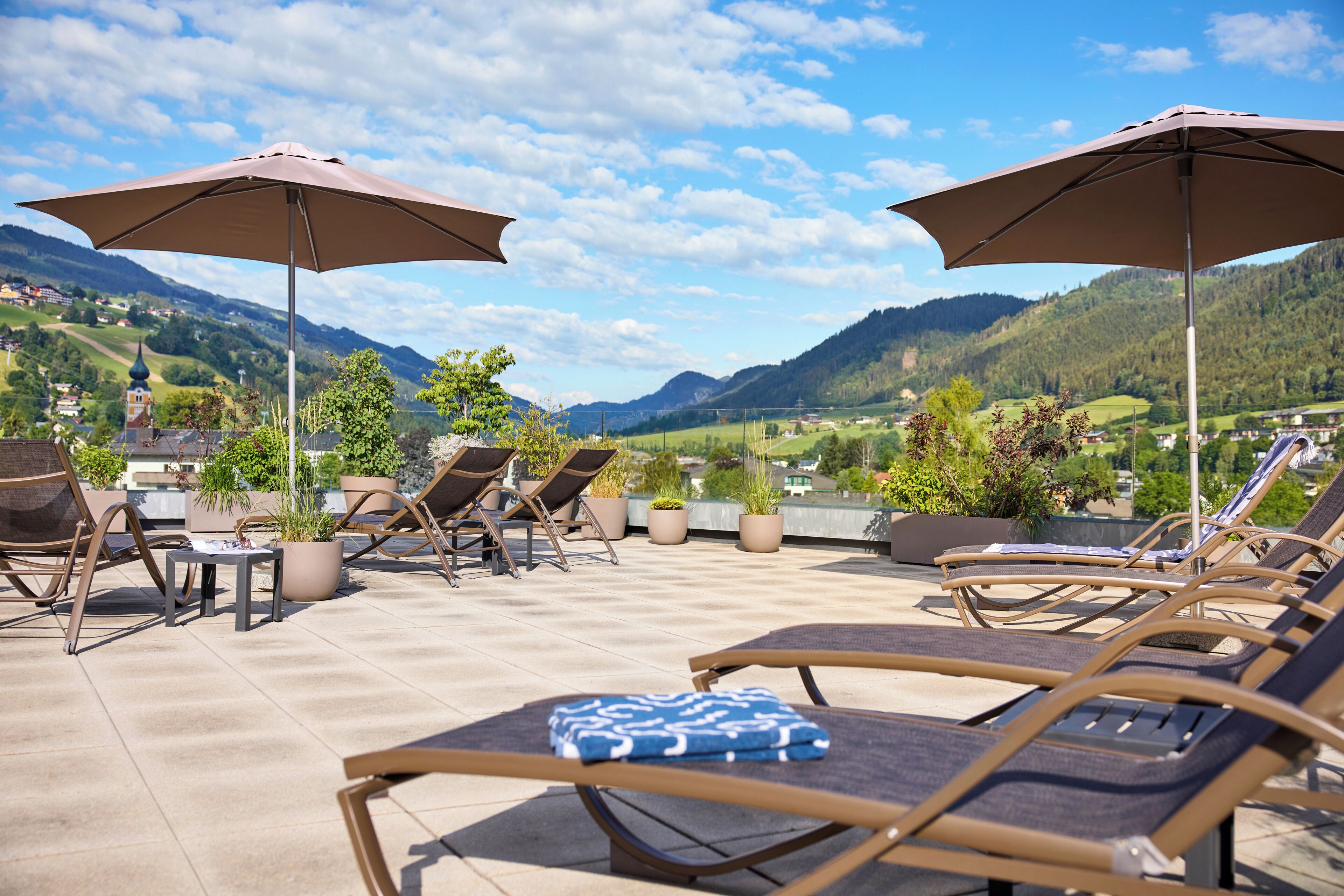 A rooftop terrace with lounge chairs and umbrellas, overlooking a mountainous landscape.