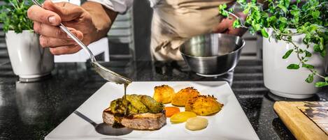 Un chef prepara un plato con carne y verduras sobre un plato blanco.