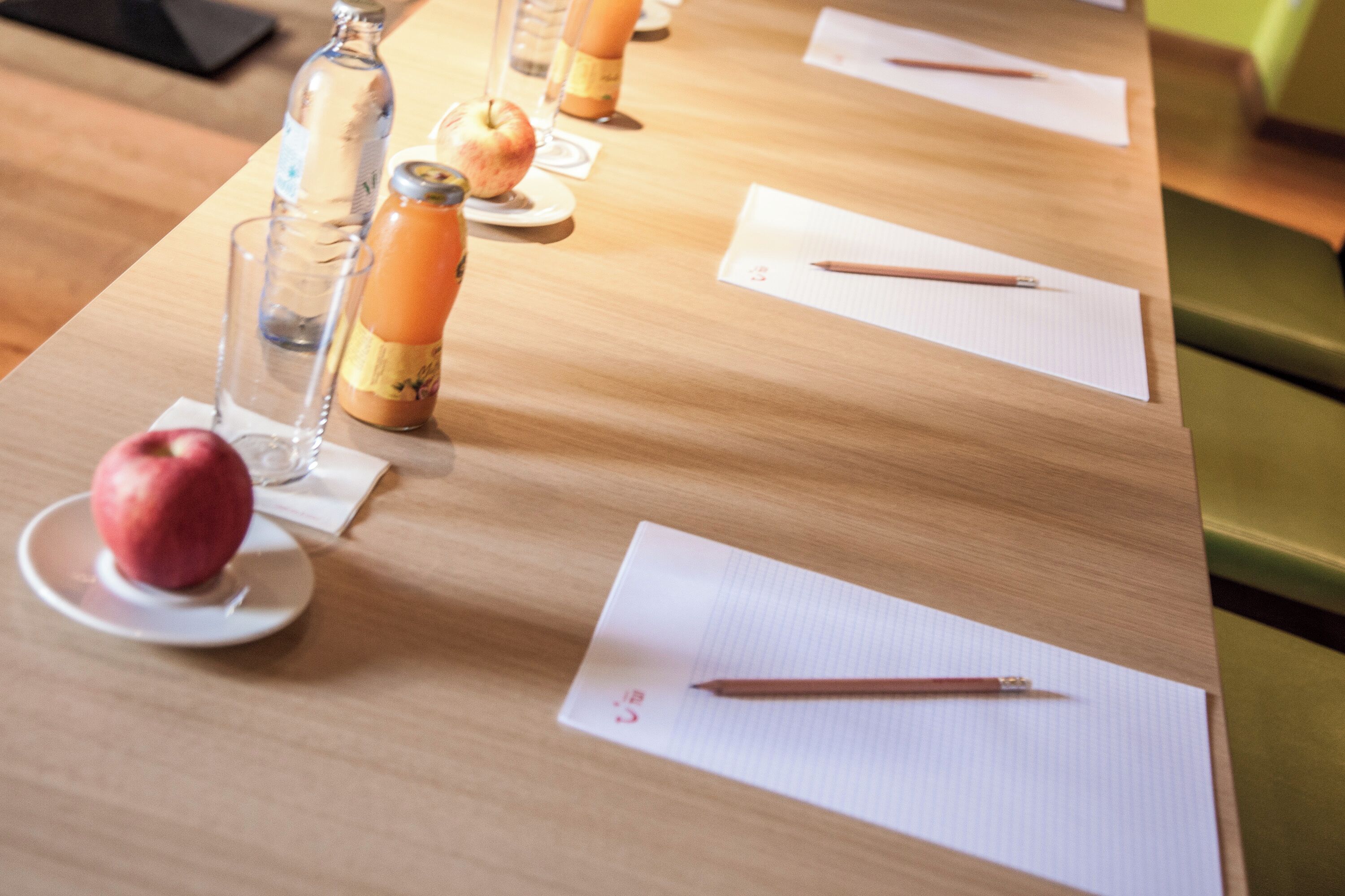 Uma mesa de madeira com um copo, uma garrafa, uma maçã e um caderno com um lápis.