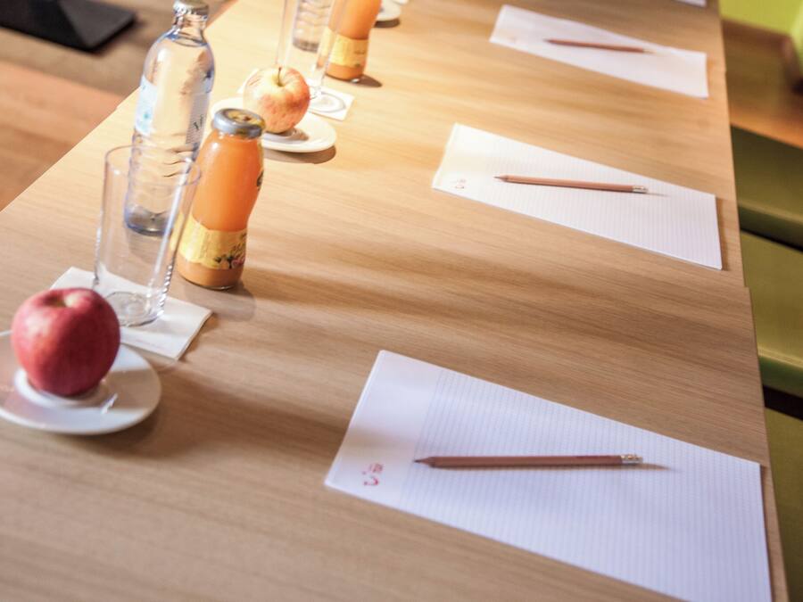 Uma mesa de madeira com um copo, uma garrafa, uma maçã e um caderno com um lápis.
