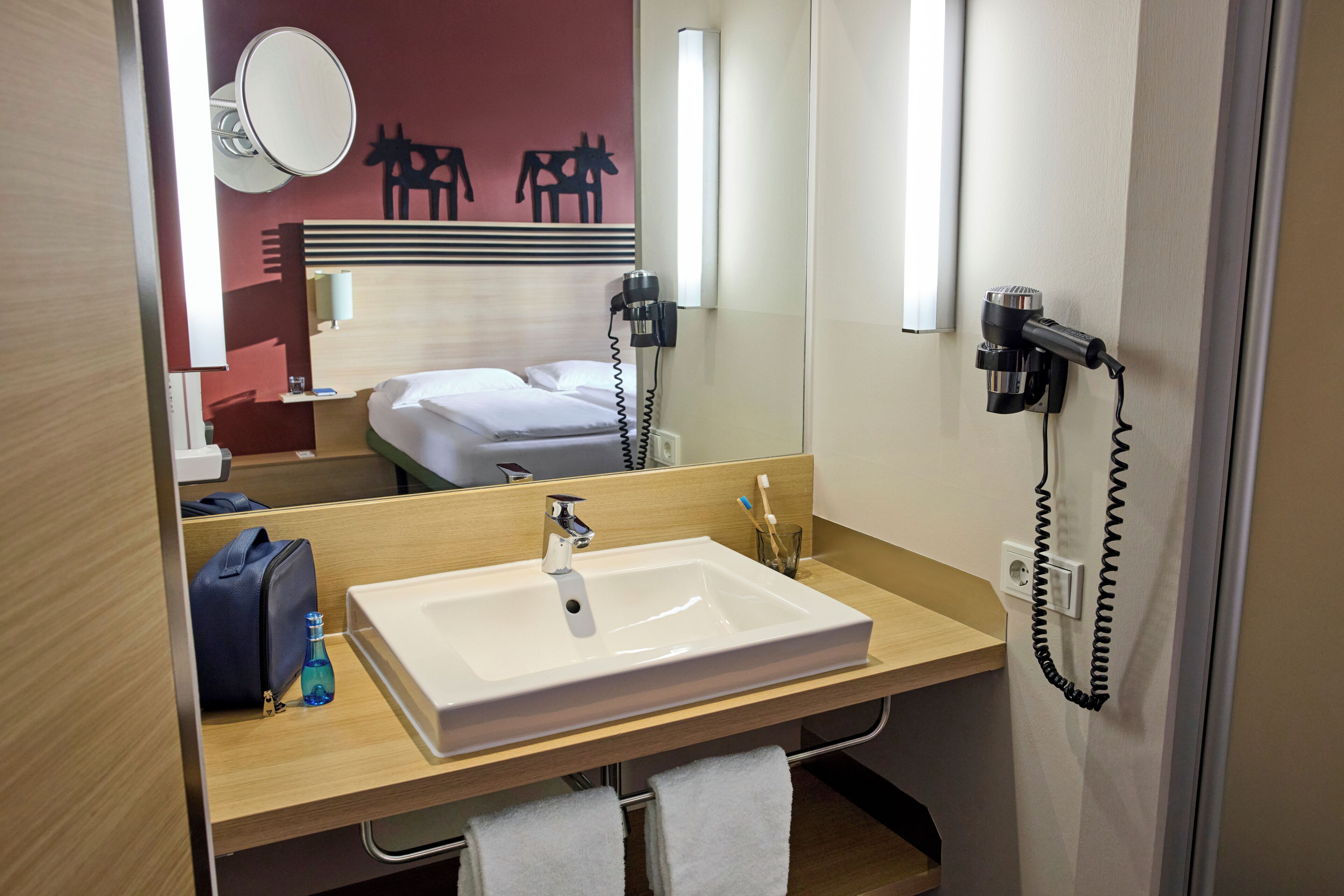 A hotel bathroom with a large sink, a mirror, a hairdryer, and a towel rack.