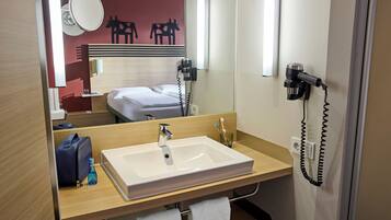 A hotel bathroom with a large sink, a mirror, a hairdryer, and a towel rack.