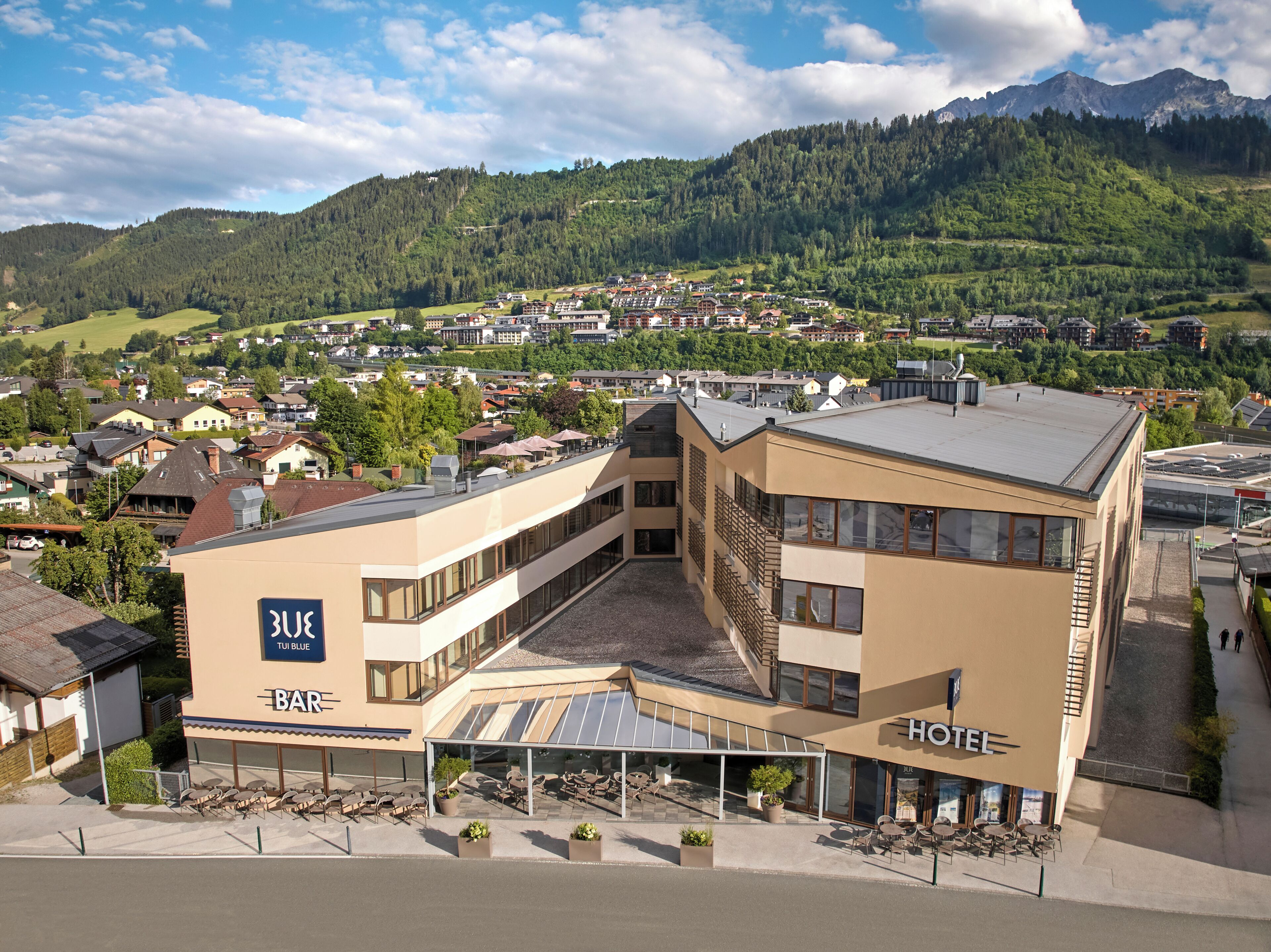 A hotel with a modern architectural design, featuring a covered outdoor seating area and a view of the surrounding town and mountains.