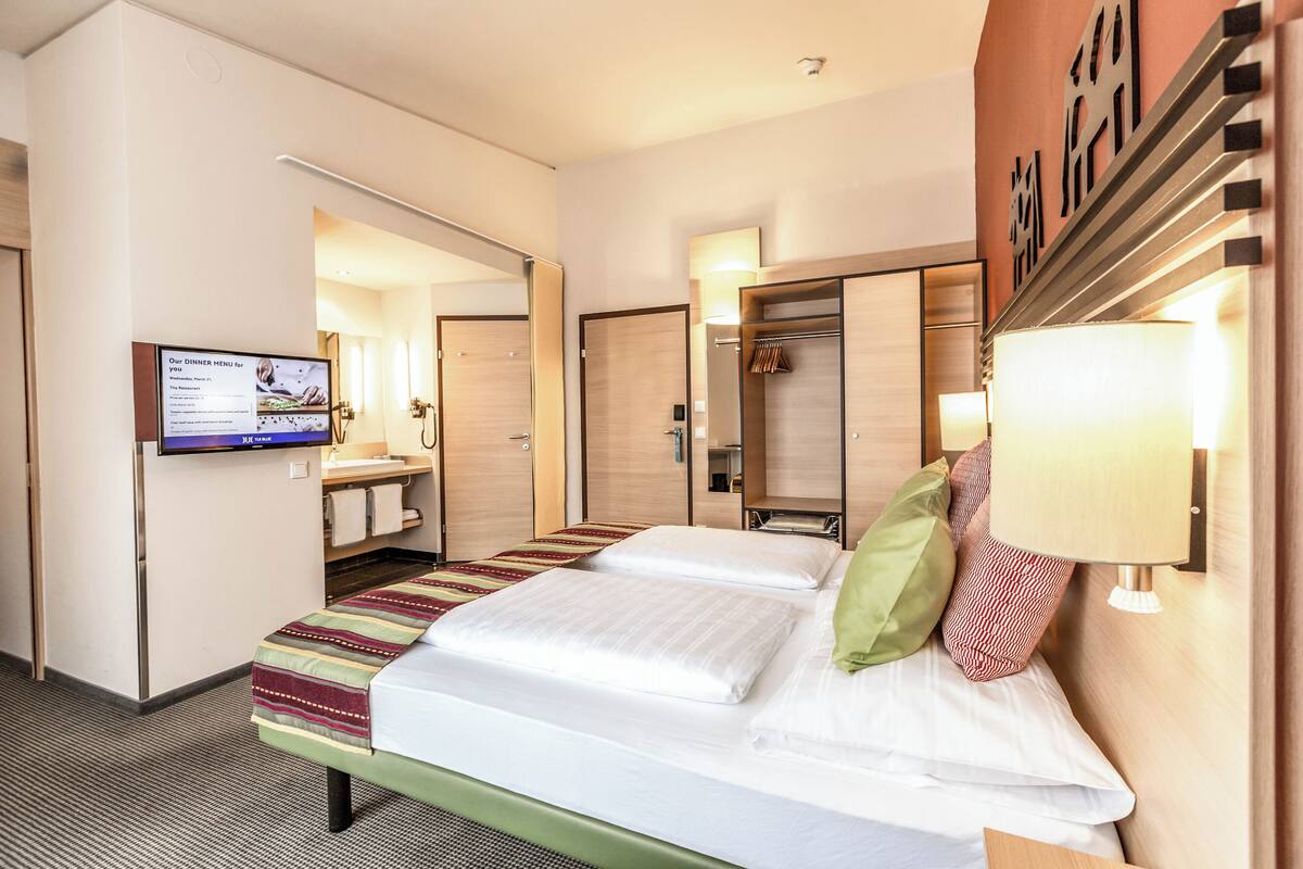 Een hotelkamer met een bed, een televisie, een kledingkast en een spiegel.