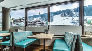 Ein Restaurant mit türkisfarbenen Polsterbänken und einem Holztisch, mit Blick auf eine verschneite Berglandschaft.