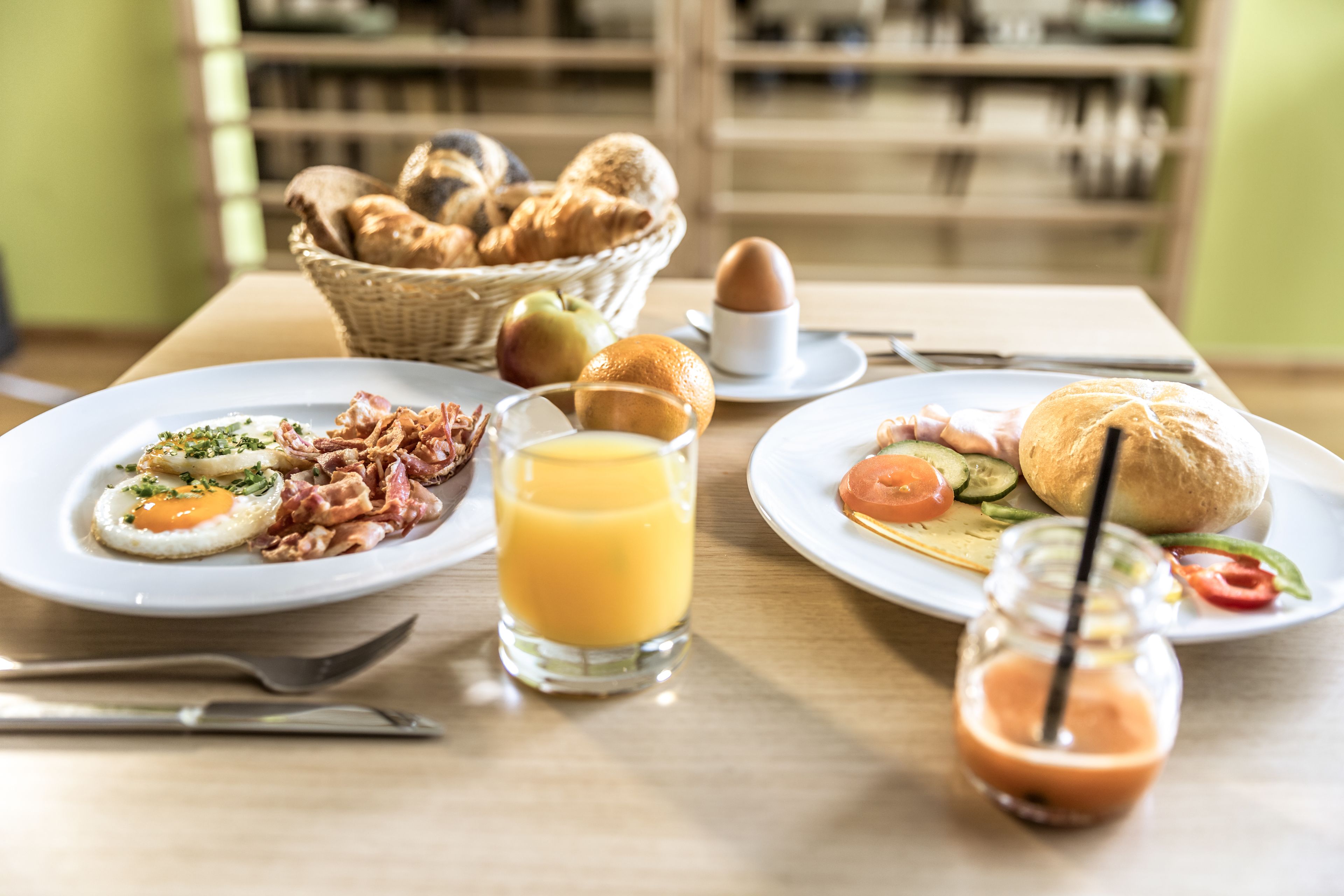 Una mesa de desayuno con platos de comida, una cesta de pan y una botella de jugo.