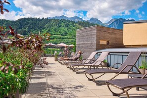 A rooftop terrace with lounge chairs, potted plants, and a view of mountains. - TUI BLUE Schladming (Schladming)
