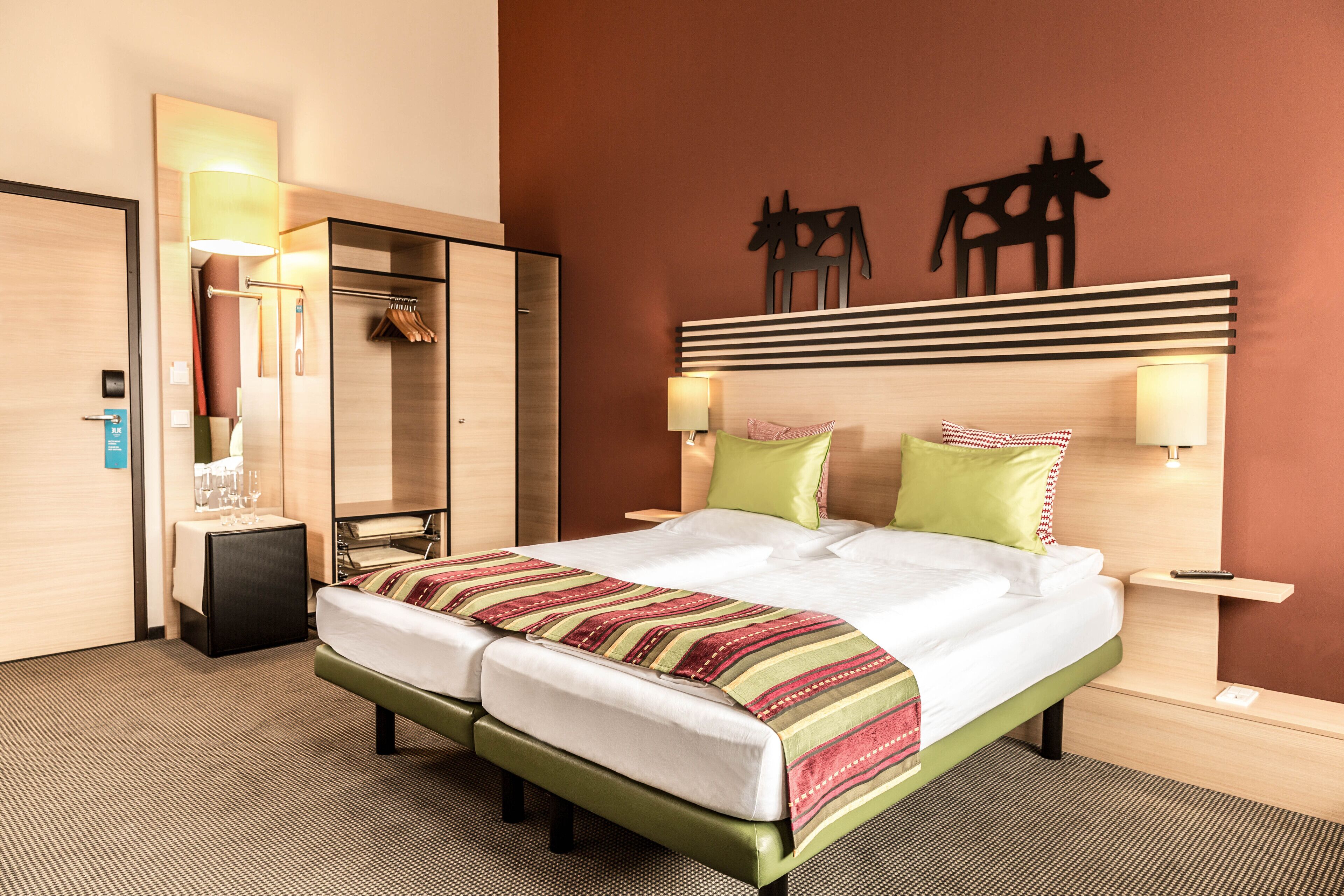 A hotel room with a double bed, a mirror, a wardrobe, and a wall-mounted artwork.