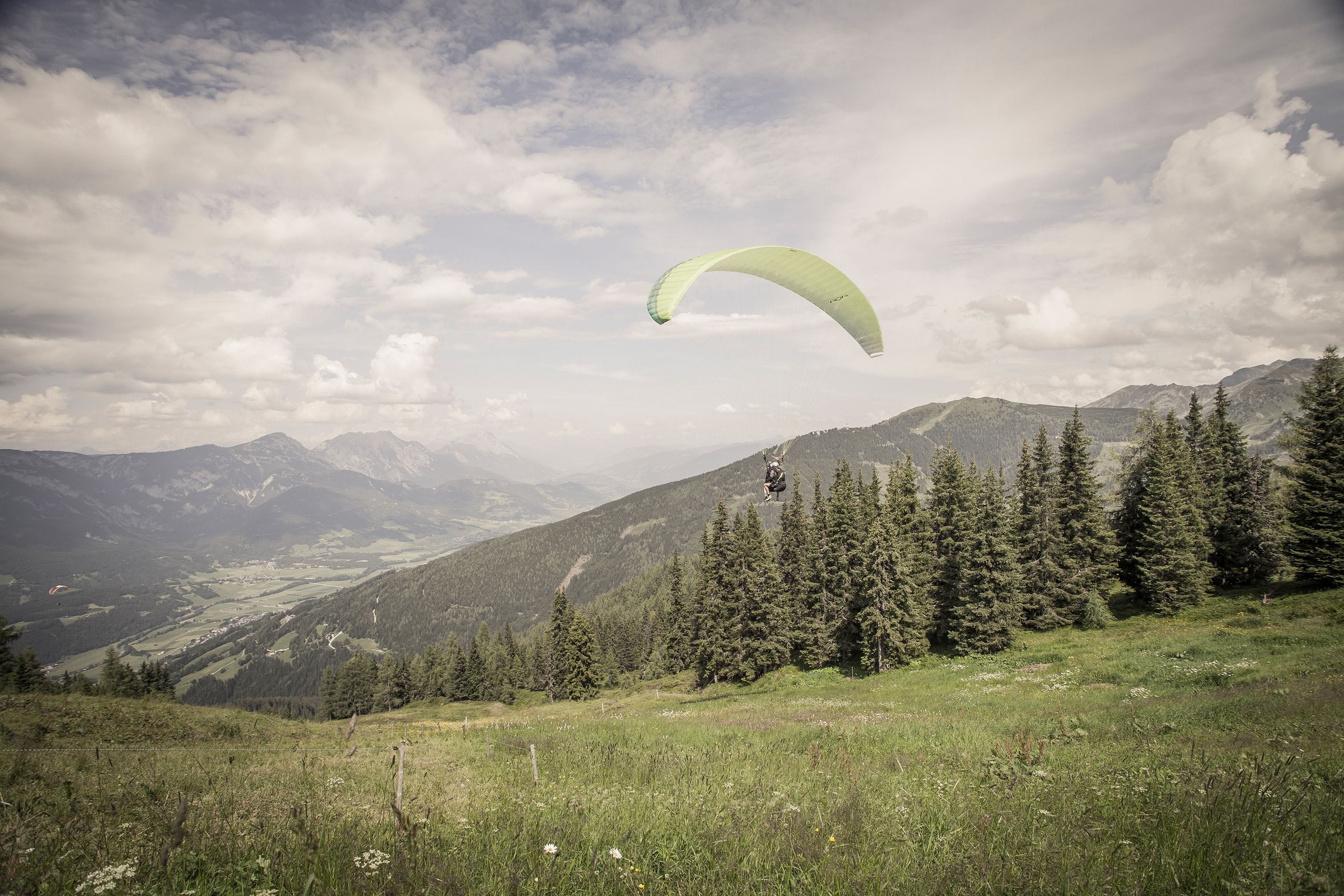 A person paragliding over a mountainous landscape with dense forests and a valley below.