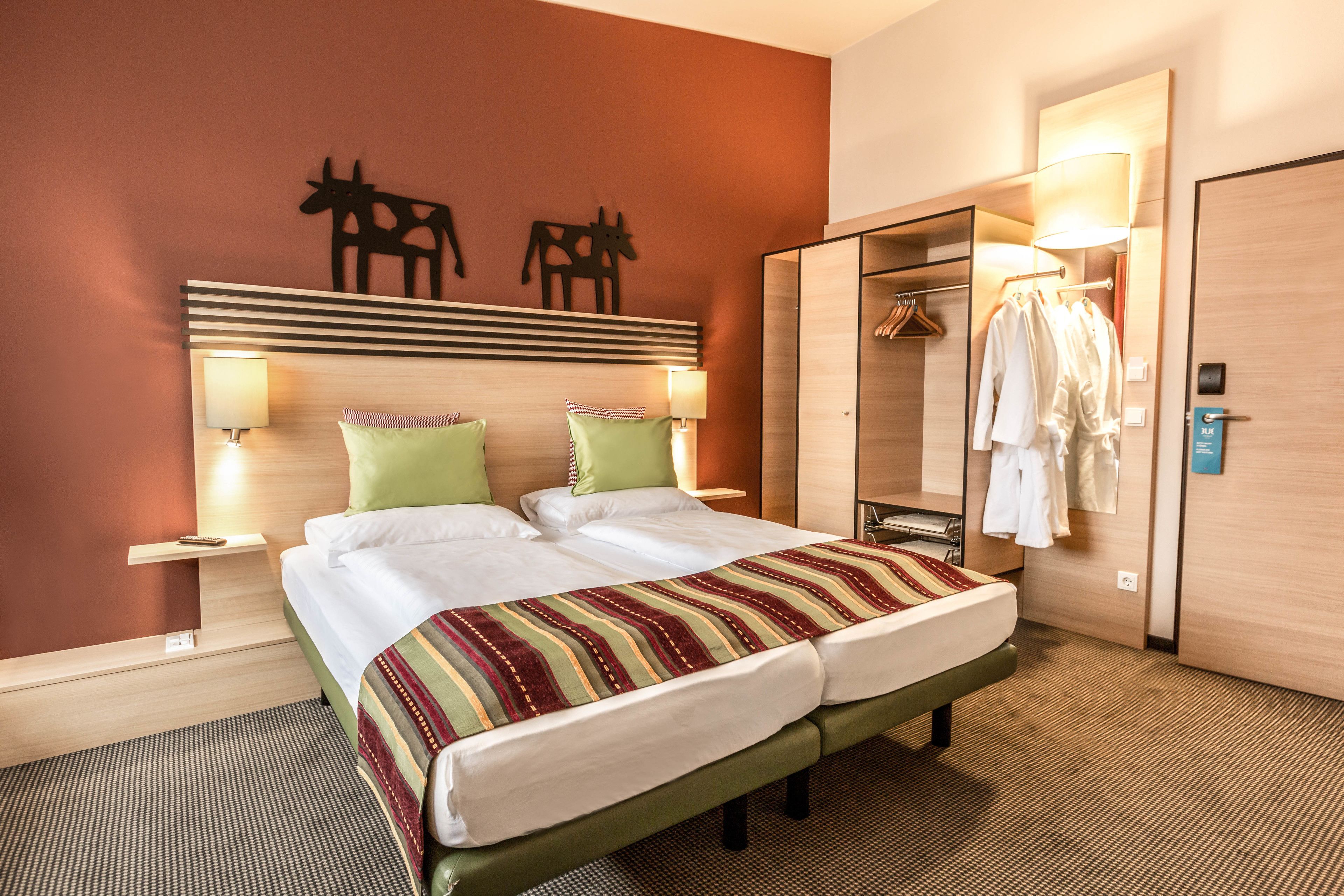 A hotel room with a bed, two nightstands with lamps, a wardrobe, and a mirror.