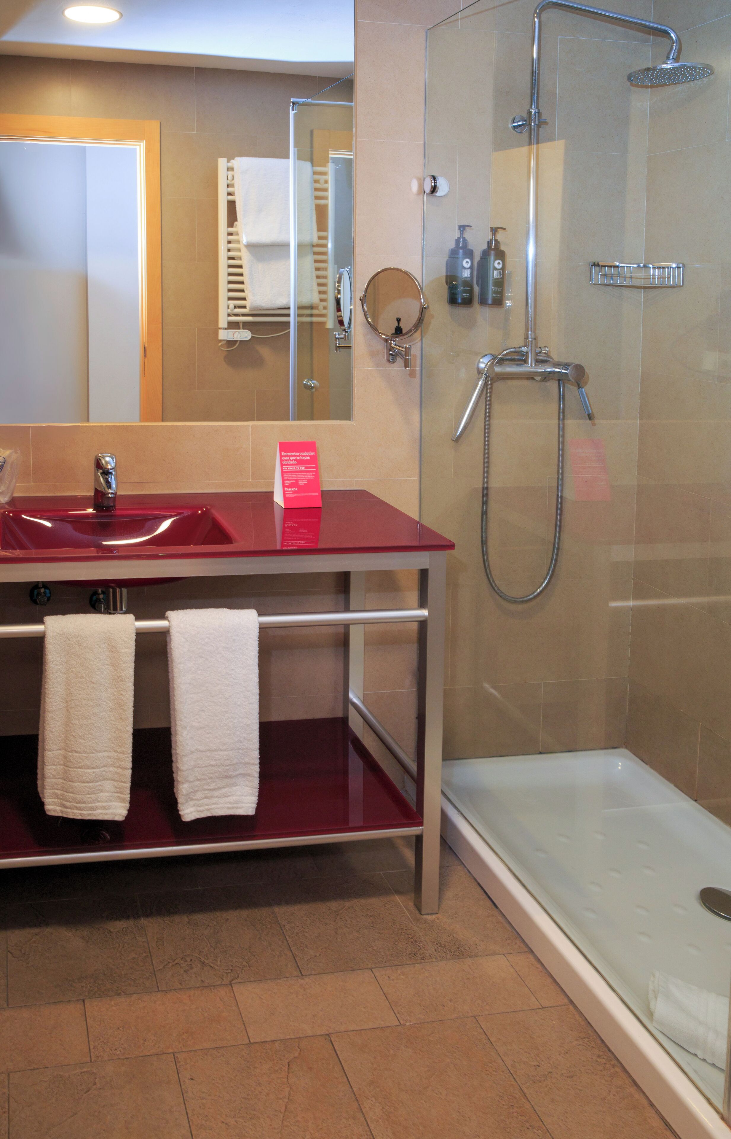Un baño con ducha de vidrio, un lavamanos rojo y un espejo.