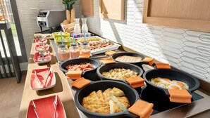 Un bufé con diversos platos y bebidas, incluyendo tortillas, huevos revueltos y fruta.