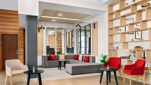 Un vestíbulo moderno con un sofá seccional gris, sillones rojos y una mesa de centro negra. Hay varias estanterías con objetos decorativos y un espejo grande.