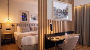 Una habitación de hotel con cama, mesita de noche, escritorio, silla y una obra de arte colgada en la pared.