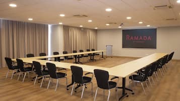 Un salón de conferencias con una larga mesa, sillas negras, una pantalla proyectora que muestra