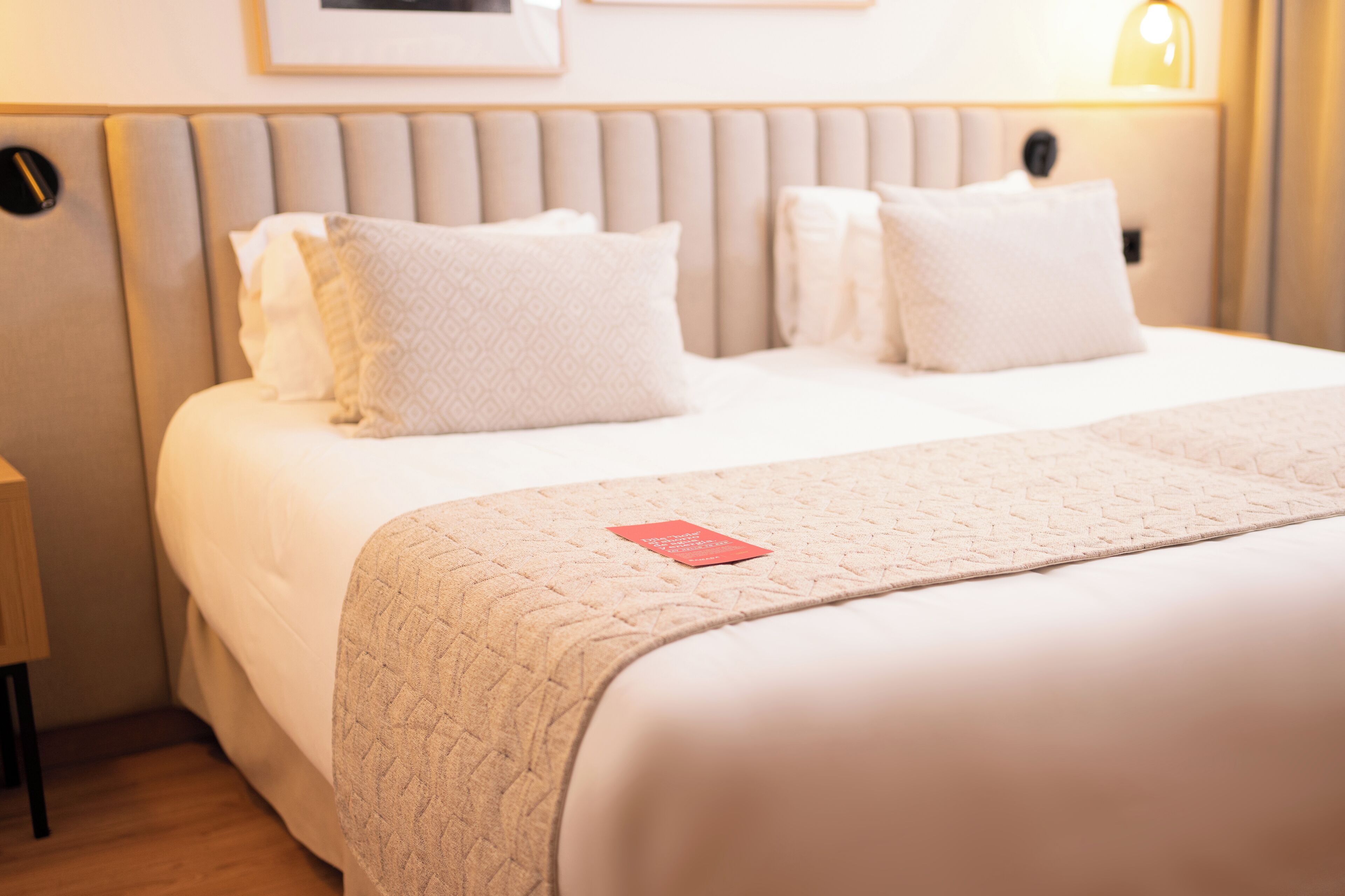 Ein ordentlich bezogenes Bett mit einem Etikett, ein Kopfteil mit einem runden Design und ein Nachttisch mit einer Lampe.