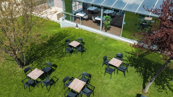 Un área de comedor al aire libre con mesas y sillas, rodeada por un césped cuidado y árboles.