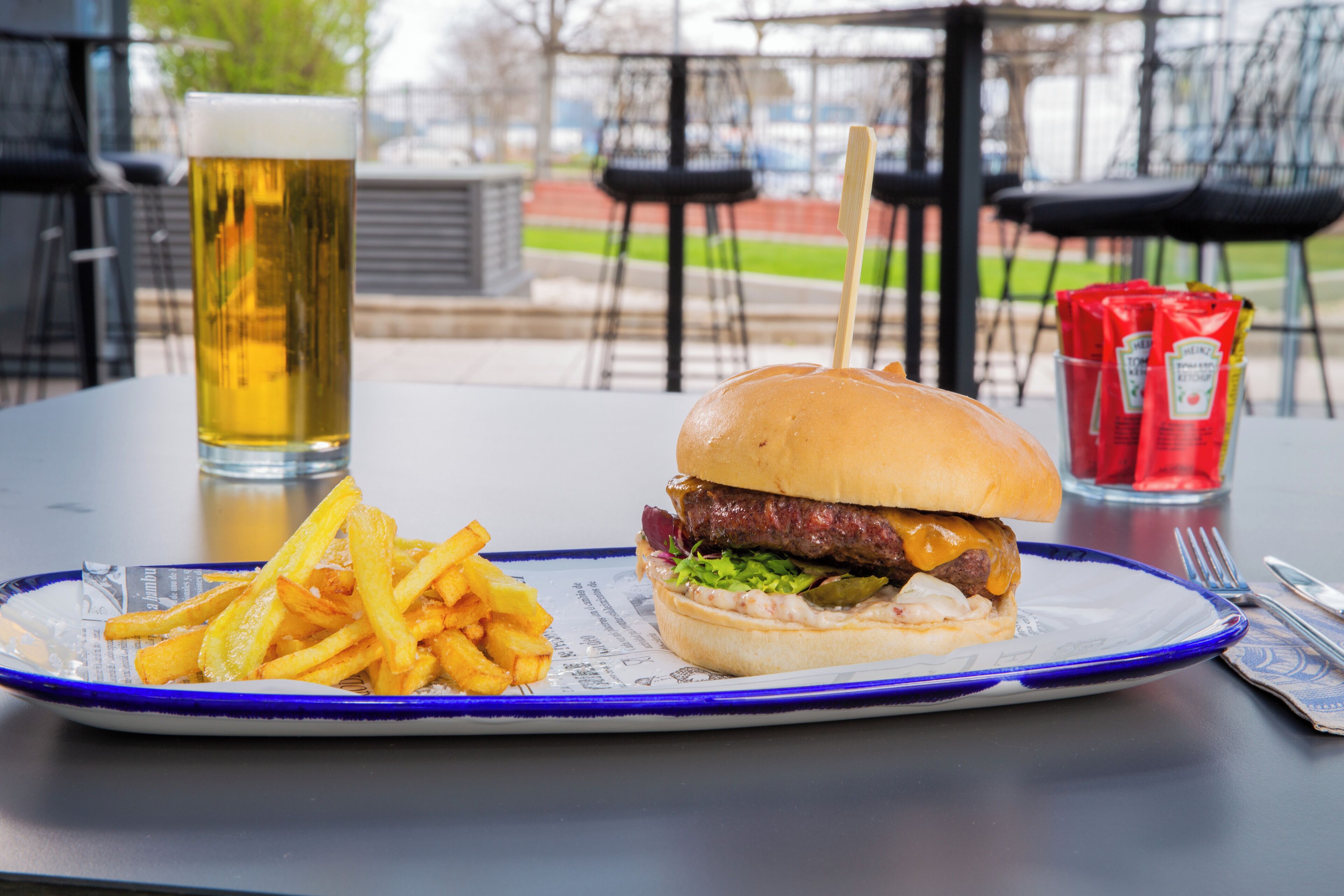 A meal consisting of a hamburger, fries, and a beer on a table.