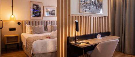 Una habitación de hotel con cama, mesita de noche, escritorio, silla y dos cuadros en la pared.