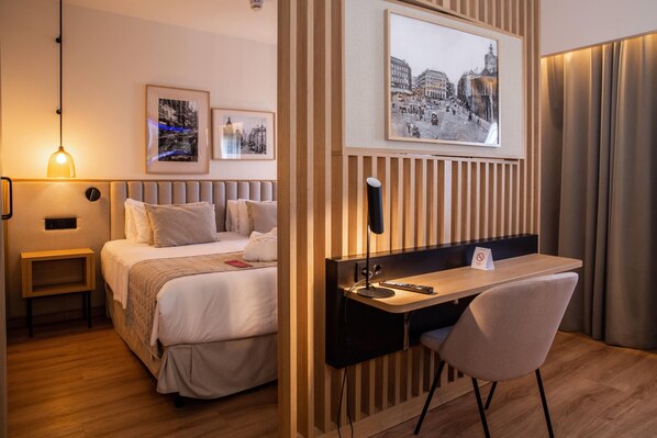 Una habitación de hotel con cama, mesita de noche, escritorio, silla y dos cuadros en la pared.